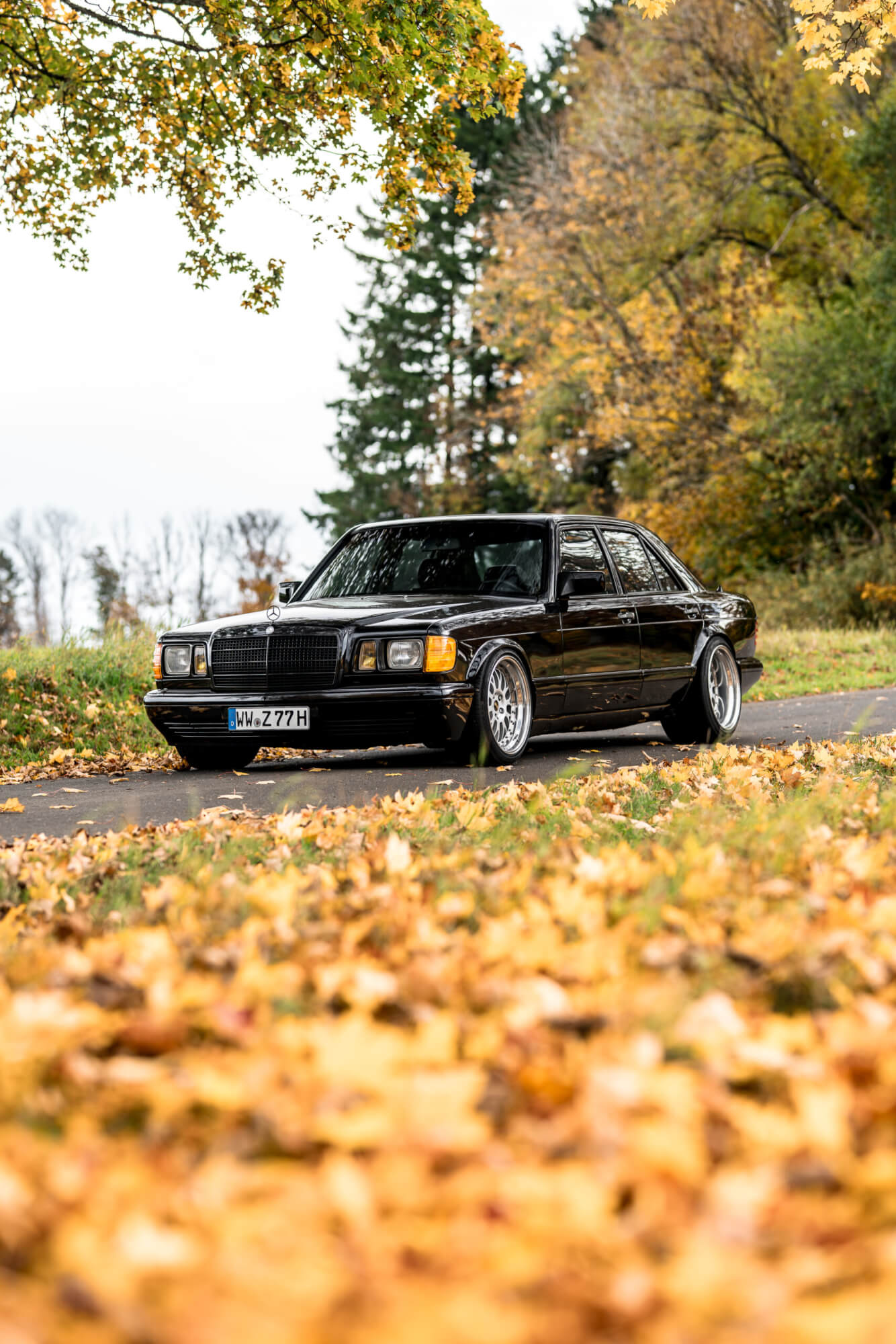 Schwarzer Mercedes-Benz W126 von Inden Design auf einer herbstlichen Straße